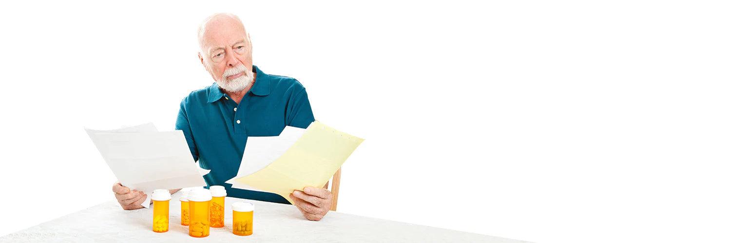 Senior man reviewing prescription papers and pill bottles at home, illustrating common medication management struggles.