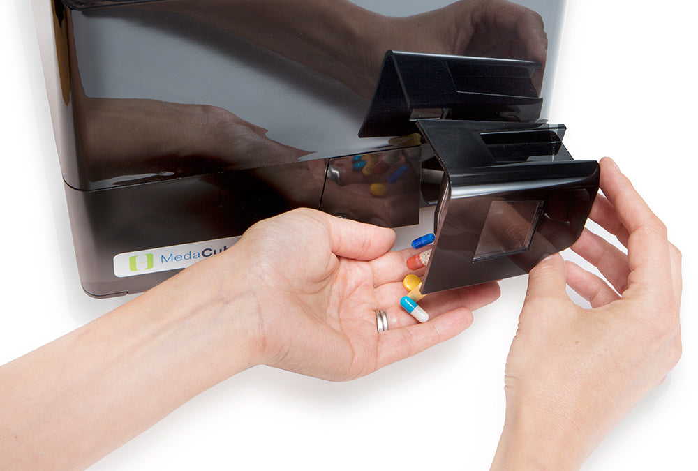 Hand turning MedaCube dispense drawer and pouring medications into another hand. 